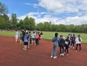 Eine Schulklasse steht auf einem Sportolaz an einer Lufbahn